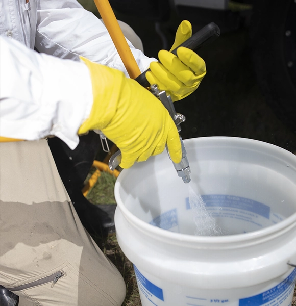 person wearing gloves mixing pesticide in a bucket